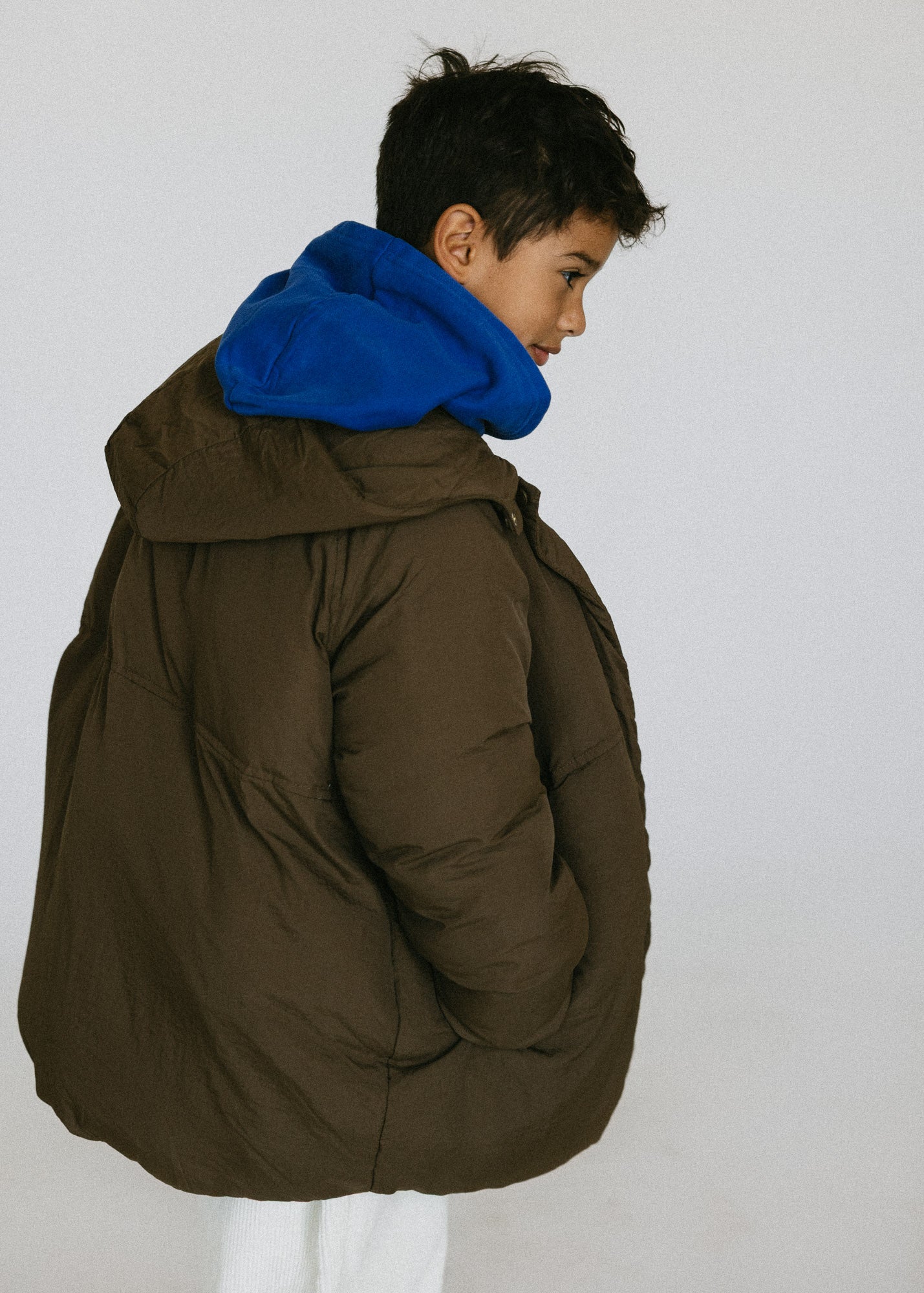 Back and side view of a child wearing a brown puffer jacket over a blue hoodie.